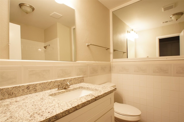 bathroom with tiled shower, toilet, tile walls, and vanity