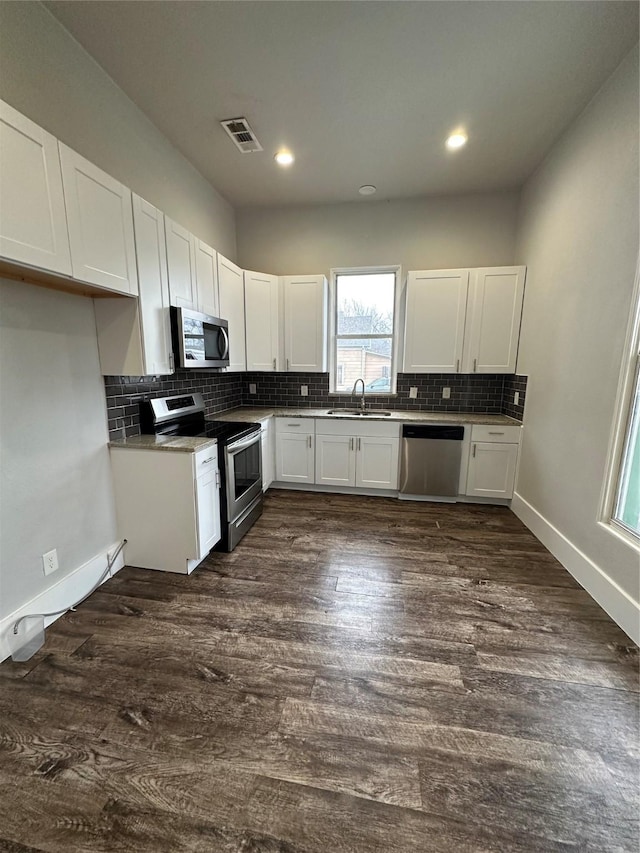 kitchen with dark wood-type flooring, sink, white cabinetry, stainless steel appliances, and backsplash