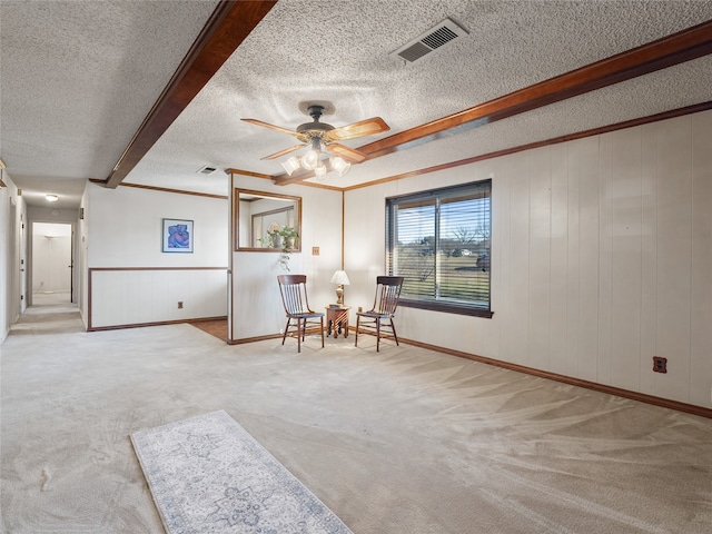 living area with wooden walls, ceiling fan, a textured ceiling, beamed ceiling, and light colored carpet