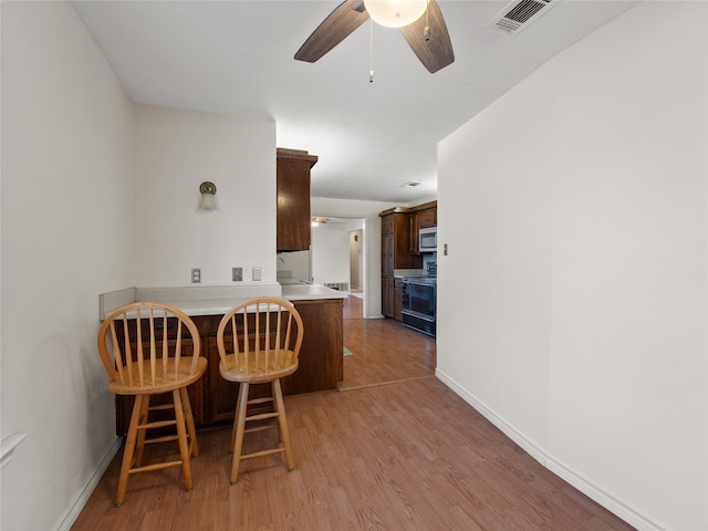 kitchen with kitchen peninsula, a kitchen bar, ceiling fan, light hardwood / wood-style flooring, and black range with electric stovetop