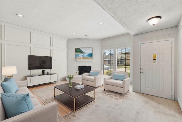 living room with a brick fireplace, a textured ceiling, and light wood-type flooring