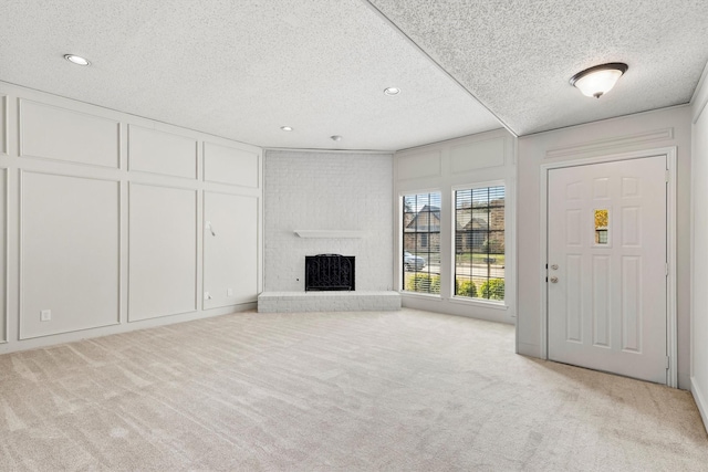 unfurnished living room with light colored carpet, a fireplace, and a textured ceiling