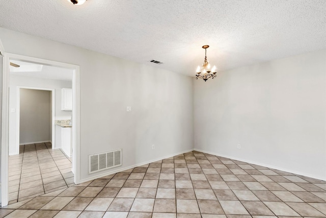 tiled empty room featuring a textured ceiling and a chandelier