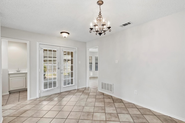 tiled empty room featuring sink, french doors, a chandelier, and a textured ceiling