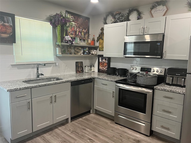 kitchen with light stone countertops, sink, light hardwood / wood-style flooring, backsplash, and appliances with stainless steel finishes