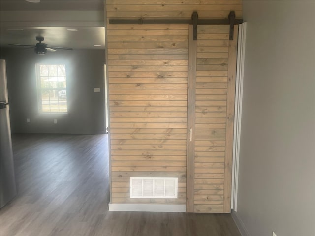 unfurnished room with a barn door, visible vents, ceiling fan, and wood finished floors