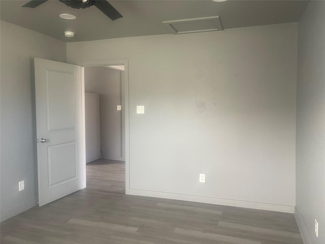 unfurnished room featuring attic access, ceiling fan, baseboards, and wood finished floors