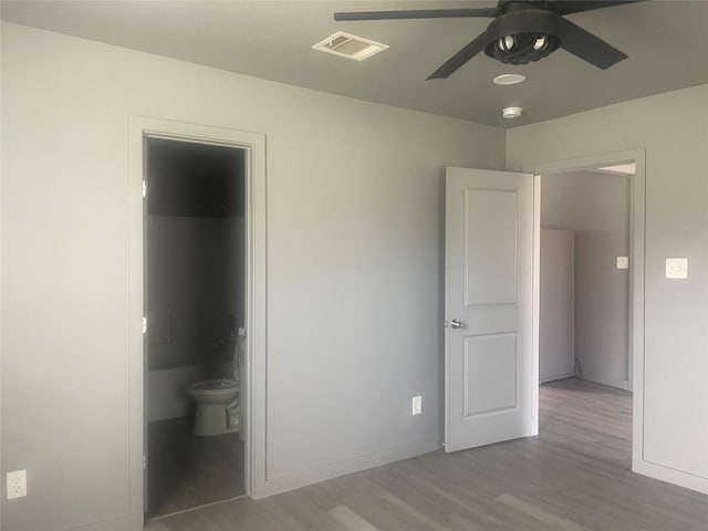 unfurnished bedroom with ensuite bath, baseboards, visible vents, and wood finished floors