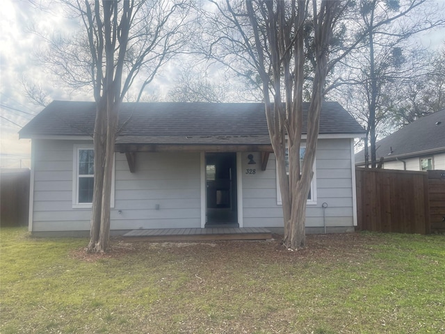 view of front of home with a front lawn, roof with shingles, and fence