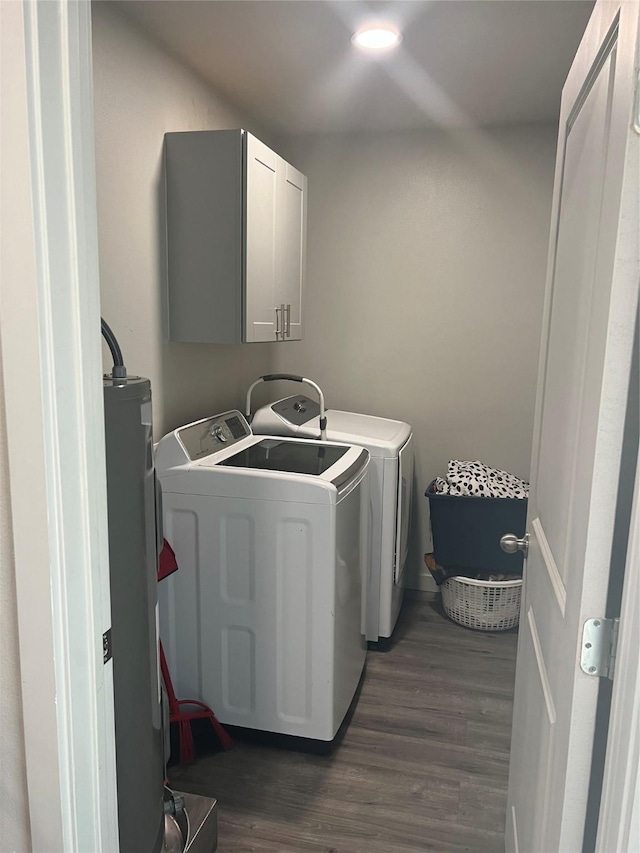 clothes washing area with cabinet space, dark wood finished floors, washing machine and clothes dryer, and water heater