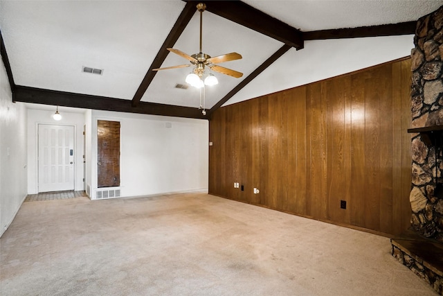 unfurnished living room with carpet flooring, ceiling fan, lofted ceiling with beams, wood walls, and a fireplace