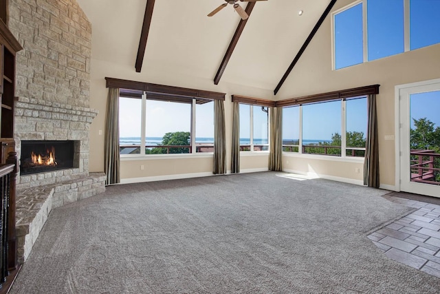 unfurnished living room featuring high vaulted ceiling, a stone fireplace, a water view, beam ceiling, and carpet floors