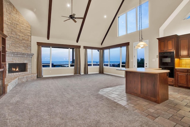 kitchen featuring light colored carpet, double oven, a water view, high vaulted ceiling, and a stone fireplace