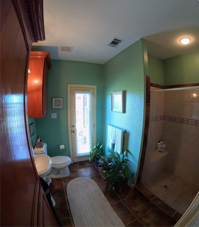 bathroom featuring tile patterned flooring, toilet, and a tile shower