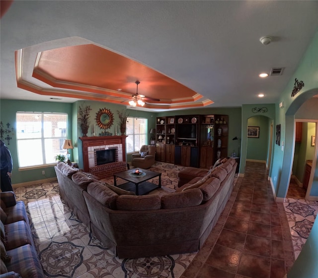 tiled living room featuring a tray ceiling, ceiling fan, and a healthy amount of sunlight