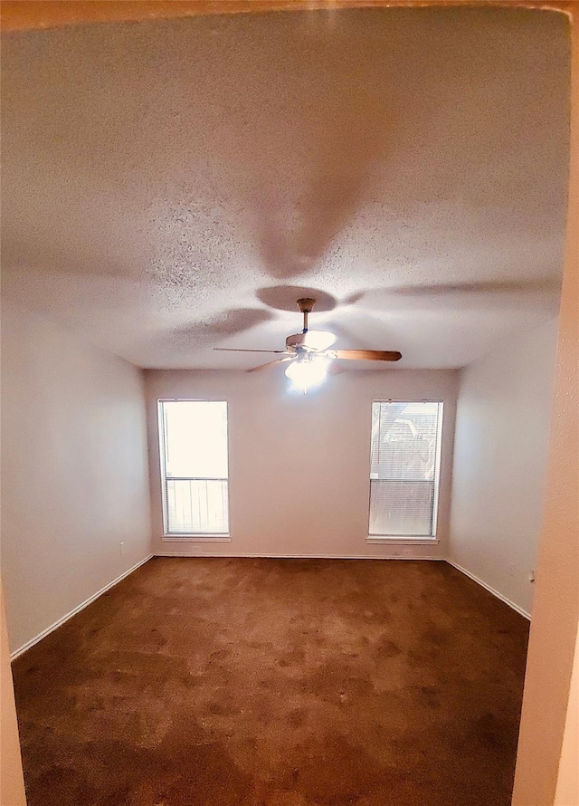 spare room with a textured ceiling, dark carpet, and ceiling fan