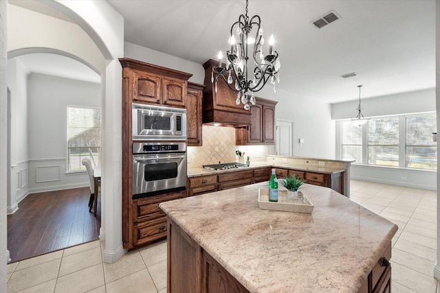 kitchen with stainless steel appliances, light tile patterned floors, a kitchen island, pendant lighting, and a notable chandelier