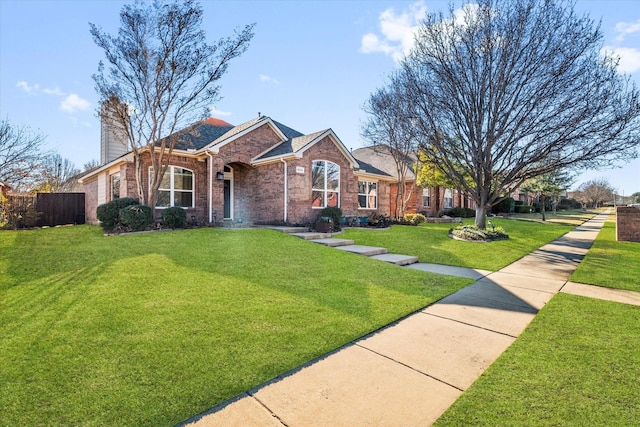 ranch-style home with brick siding, fence, a chimney, and a front lawn