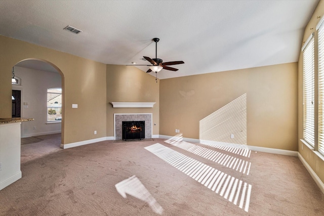 unfurnished living room with visible vents, arched walkways, a tiled fireplace, light colored carpet, and vaulted ceiling