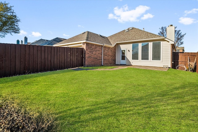 back of house with brick siding, a lawn, a shingled roof, and a fenced backyard