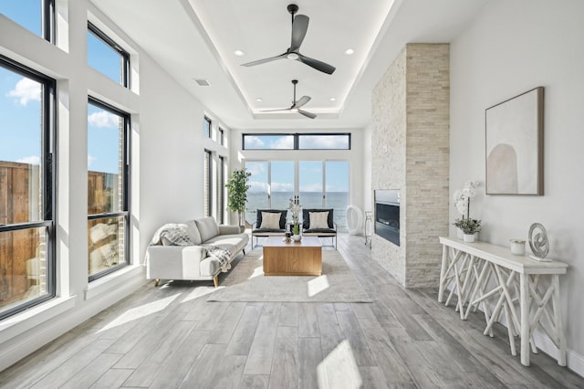 interior space featuring a water view, a raised ceiling, a wealth of natural light, and a stone fireplace