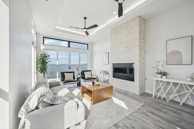 living room featuring a water view, a towering ceiling, a fireplace, a tray ceiling, and light hardwood / wood-style floors