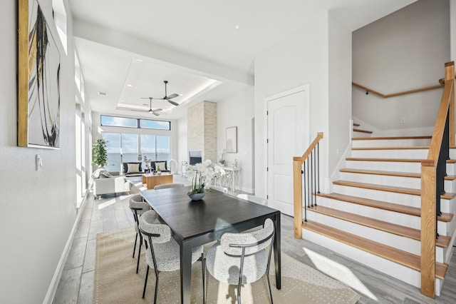 dining room featuring ceiling fan, a stone fireplace, and a tray ceiling