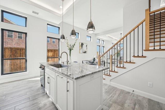 kitchen with light stone countertops, sink, decorative light fixtures, a center island with sink, and white cabinets