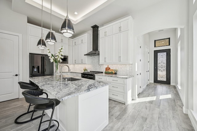 kitchen featuring white cabinets, a raised ceiling, wall chimney range hood, sink, and appliances with stainless steel finishes