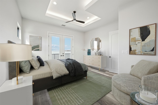 bedroom featuring access to outside, french doors, a raised ceiling, ceiling fan, and wood-type flooring