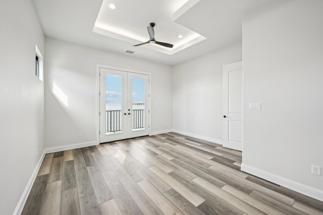 empty room with french doors, light hardwood / wood-style floors, a raised ceiling, and ceiling fan