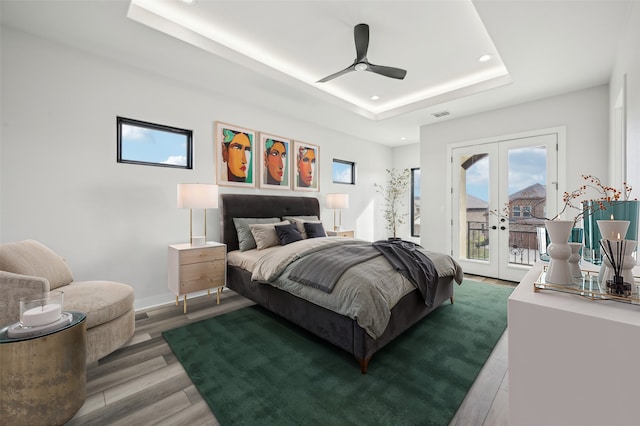 bedroom featuring french doors, ceiling fan, access to exterior, a tray ceiling, and wood-type flooring