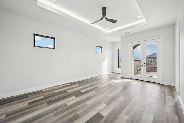 empty room with a tray ceiling, ceiling fan, french doors, and hardwood / wood-style flooring