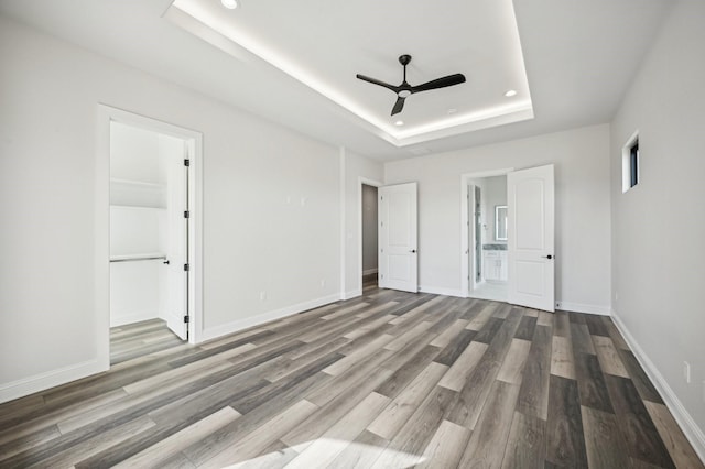 unfurnished bedroom with hardwood / wood-style flooring, ensuite bathroom, ceiling fan, and a raised ceiling