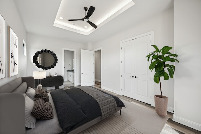 bedroom with ensuite bath, a tray ceiling, ceiling fan, wood-type flooring, and a closet