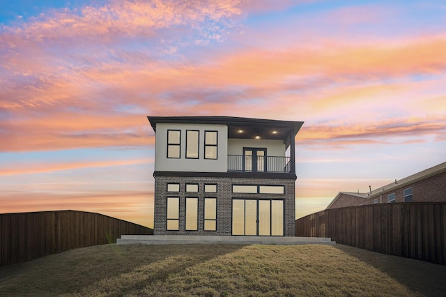 back house at dusk with a balcony and a lawn