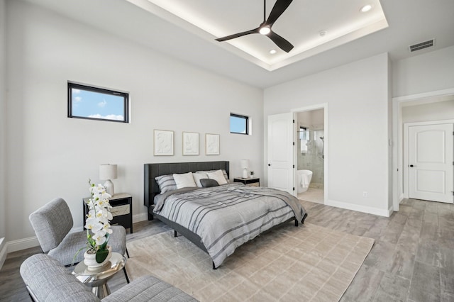 bedroom with a tray ceiling, ceiling fan, hardwood / wood-style floors, and ensuite bathroom