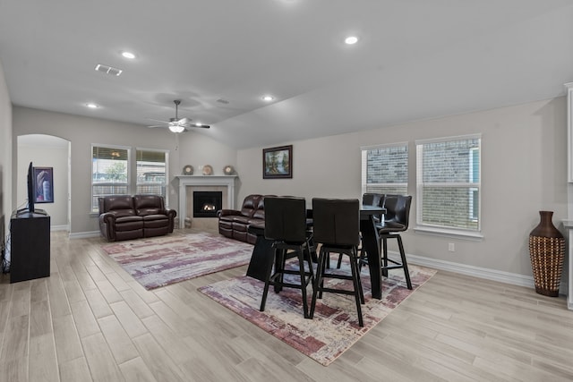 dining room featuring a fireplace, light hardwood / wood-style flooring, vaulted ceiling, and ceiling fan