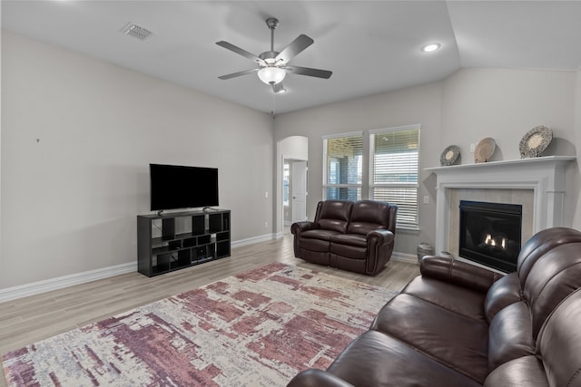 living room with a tile fireplace, vaulted ceiling, light hardwood / wood-style flooring, and ceiling fan