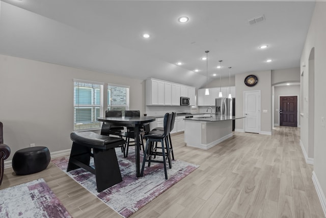 dining area with sink, vaulted ceiling, and light hardwood / wood-style flooring