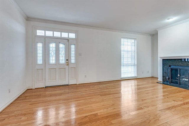 entryway with light wood-type flooring, ornamental molding, and a tile fireplace