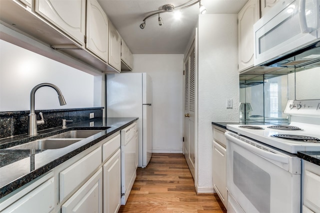 kitchen featuring sink, dark stone countertops, light hardwood / wood-style floors, white appliances, and white cabinets