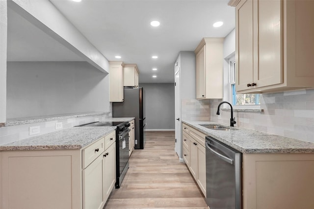 kitchen with a sink, light stone countertops, stainless steel appliances, light wood-style floors, and backsplash