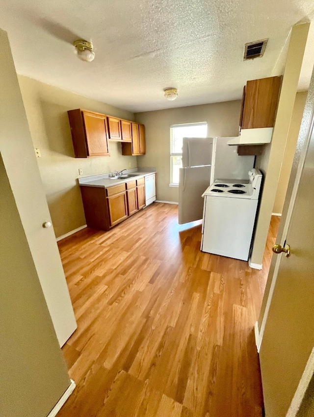 kitchen featuring light wood-type flooring, white appliances, a textured ceiling, exhaust hood, and sink