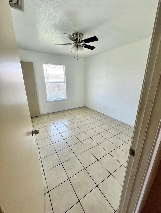 tiled empty room with ceiling fan and a textured ceiling