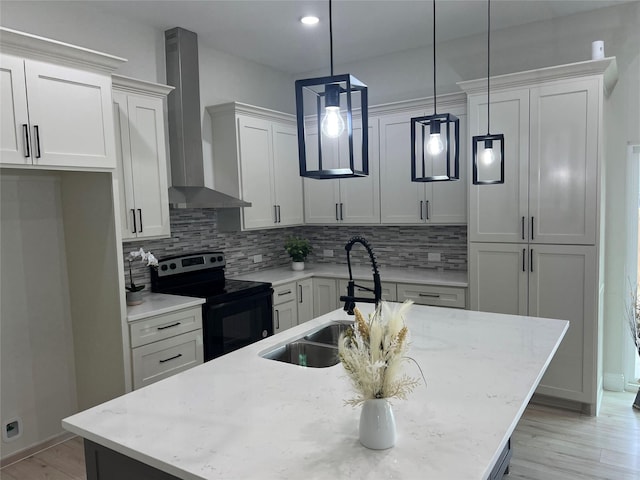 kitchen featuring wall chimney exhaust hood, a kitchen island with sink, sink, decorative light fixtures, and range with electric stovetop