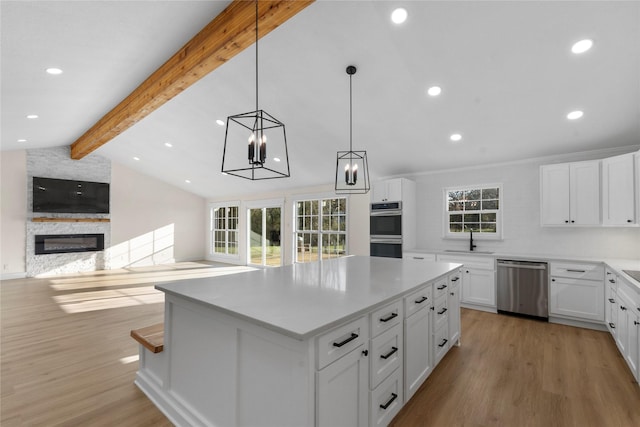 kitchen with stainless steel appliances, white cabinetry, a center island, light hardwood / wood-style floors, and a stone fireplace