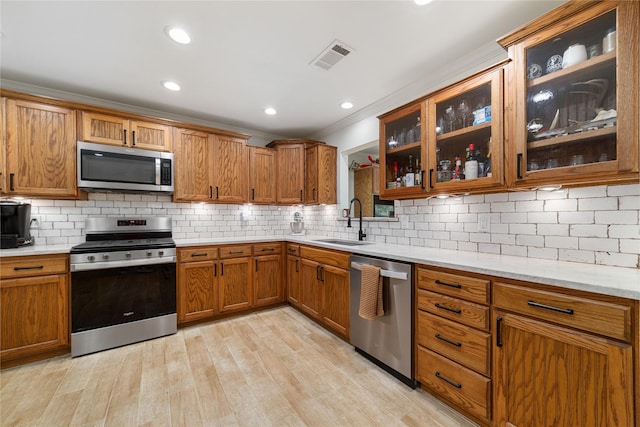 kitchen with backsplash, sink, light stone countertops, light wood-type flooring, and stainless steel appliances