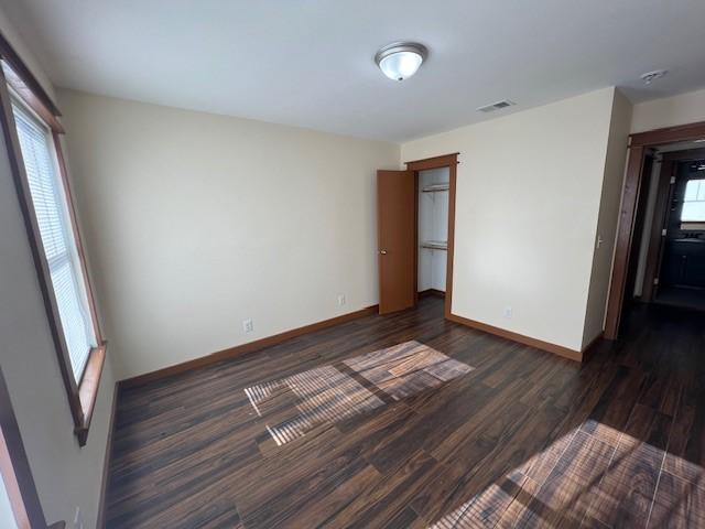 empty room with baseboards, visible vents, and dark wood-style flooring