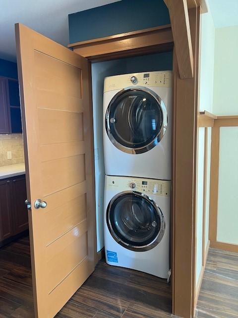 clothes washing area featuring dark wood-type flooring and stacked washer and clothes dryer